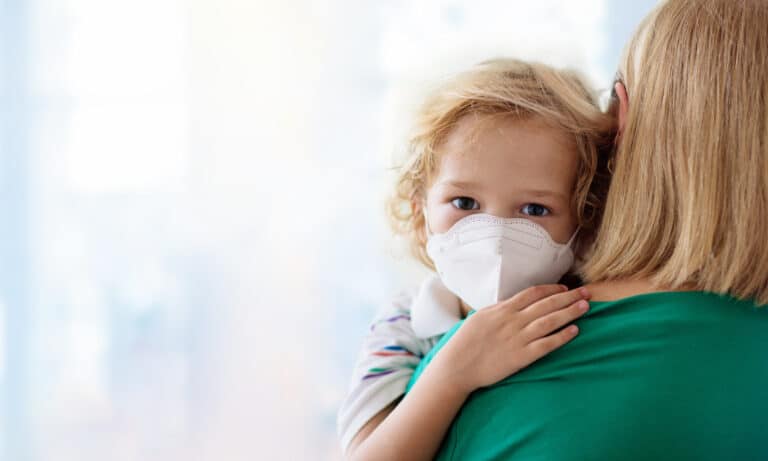 Mother carries their child who wears a white disposable face mask.