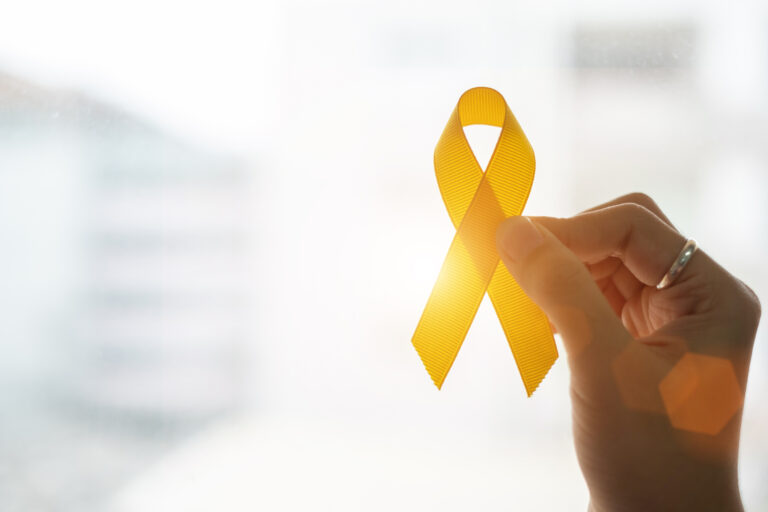 A hand holds a yellow ribbon against sunlight, in recognition and support of those living with mental illness.