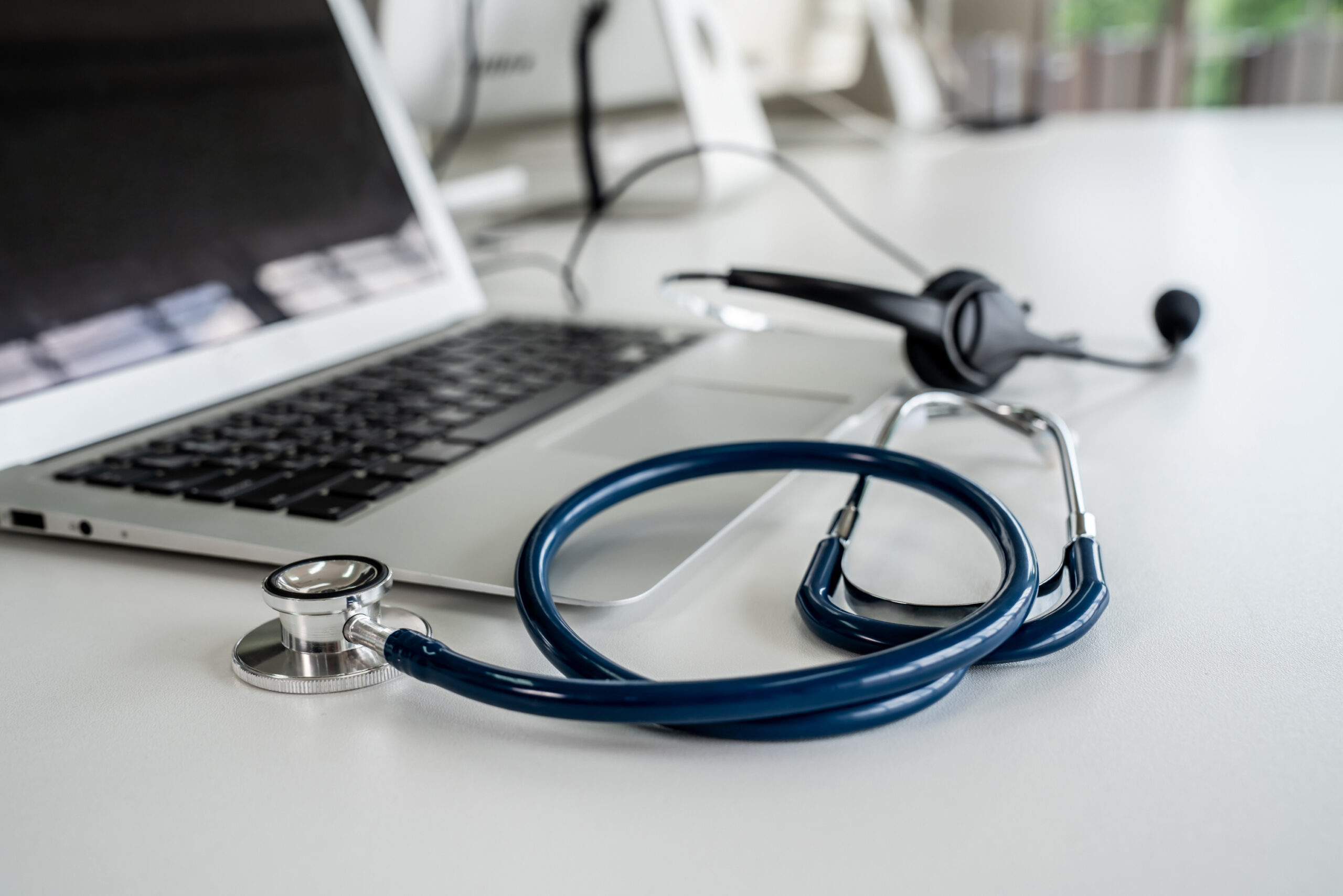 ASO concept: a laptop is positioned between a phone headset and a stethoscope, symbolizing how AI software can help Answering Service Operators relay accurate messages to providers.