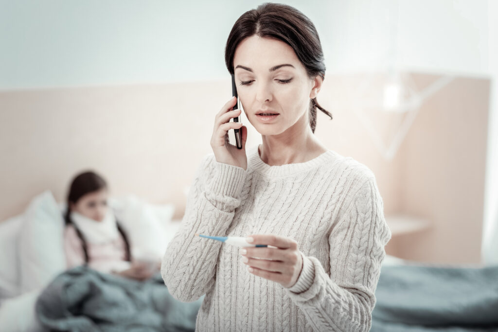TriageLogic A mother gives thermometer readings over the phone to an ASO while her daughter is resting in bed.