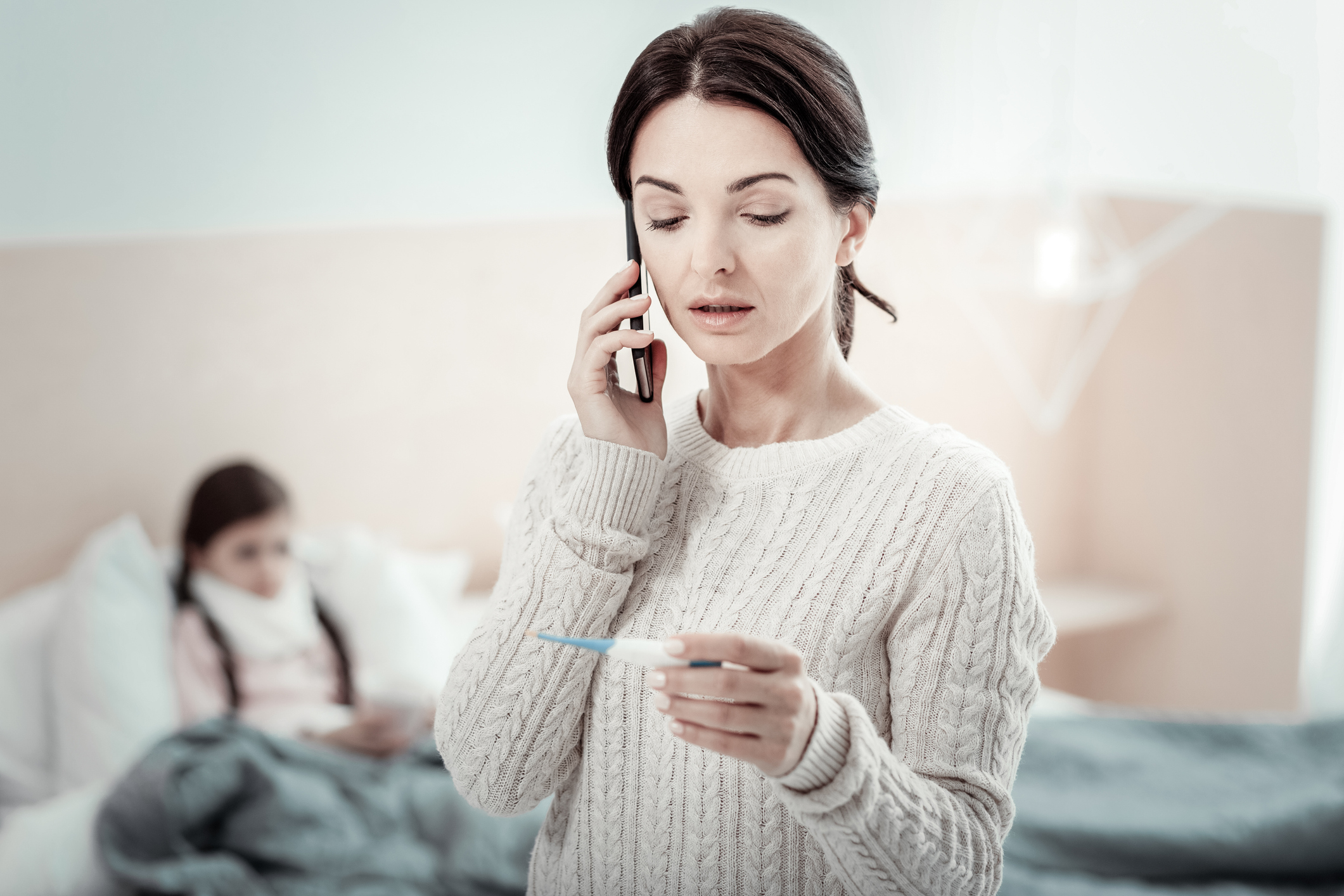 A mother gives thermometer readings over the phone to an ASO while her daughter is resting in bed.