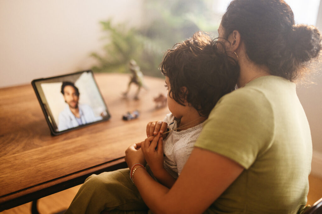 A mother and child use a tablet for a video call with their family doctor for telemedicine.