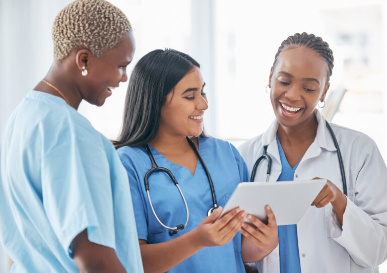 Three nurses smile while reviewing data on a tablet that shows nurse productivity and patient care.