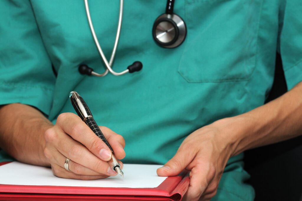 A nurse wearing a stethoscope around their neck uses a pen to fill out a paper form.