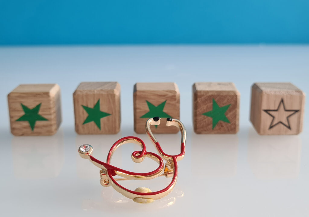 Nurse triage quality assurance concept: a small metal stethoscope is set in front of wooden blocks with green stars that represent a ratings system.