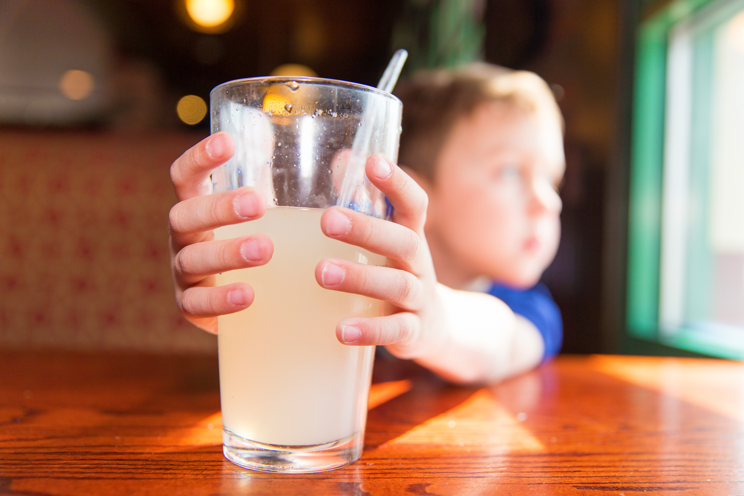 Childhood obesity concept: a young boy grips a glass filled with juice while sitting at a table and staring out the window.
