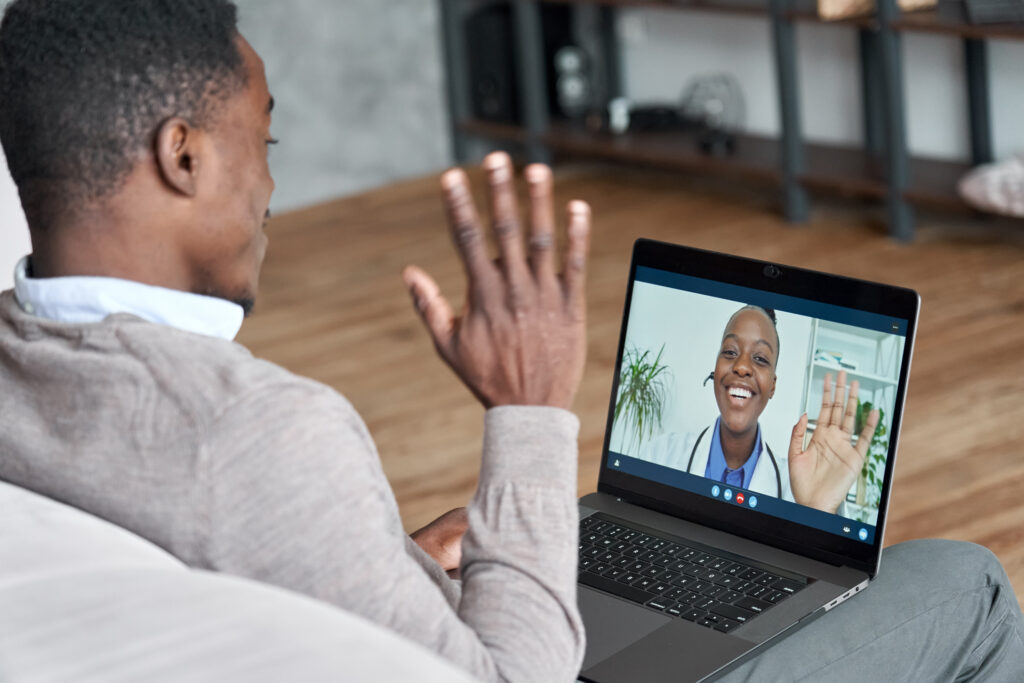 A patient waves to their provider through the screen of their laptop computer during a telehealth visit as part of remote health care.