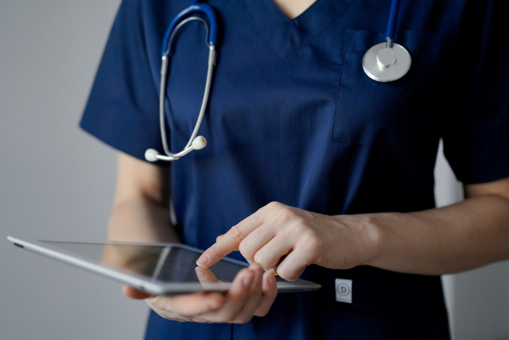 A nurse wearing a stethoscope reviews nurse triage books on her tablet.