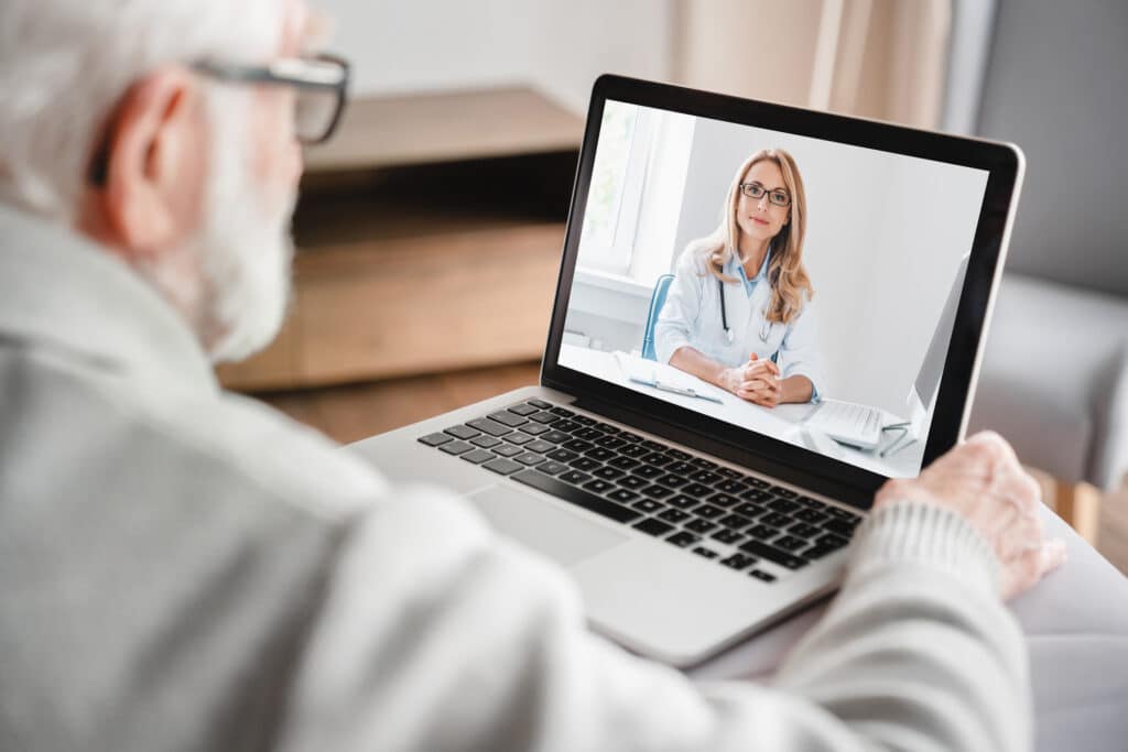 An older patient uses a laptop to talk with their doctor after scheduling an appointment with telehealth nurse triage.