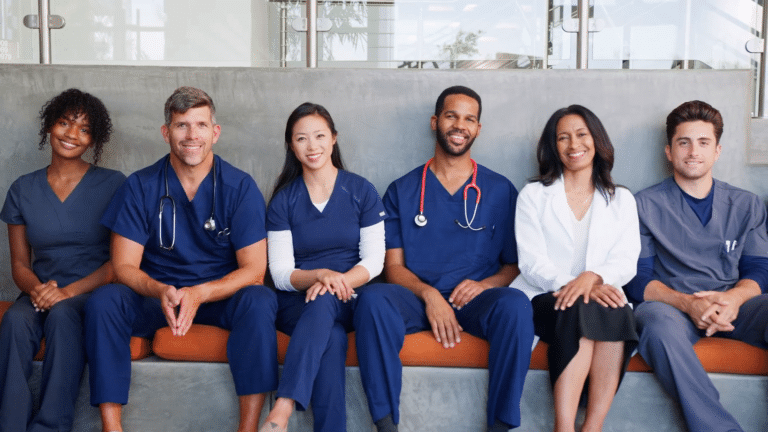 A group of healthcare professionals smile while sitting together on a bench. nurse triage on call. telehealth technology solutions. remote patient monitoring. ai in healthcare. using ai to help with triage. nurses using technology.