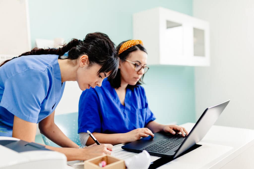 Two nurses in a doctor's office use History Assist on a laptop to share patient symptoms with their provider.