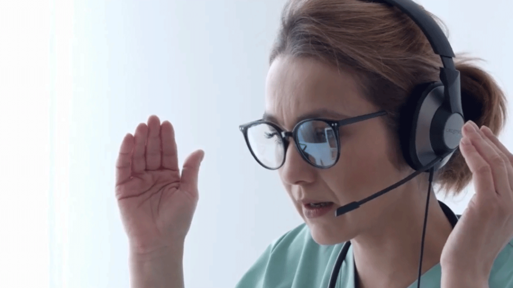 A triage nurse speaks with a patient using headphones and telehealth video conferencing.