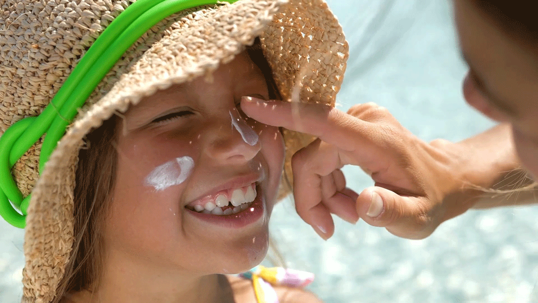 A parent rubs sunscreen on their smiling child's face while they're at the pool.