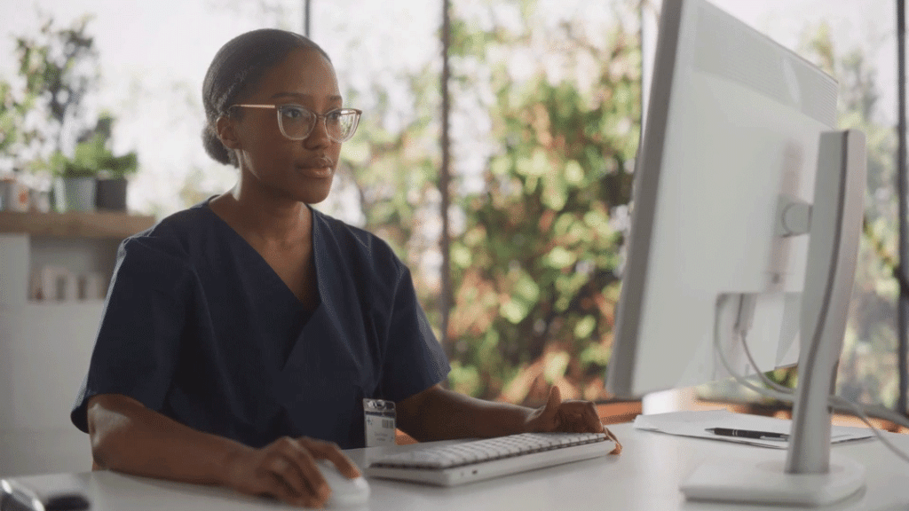 A nurse sitting at ther desk uses nurse triage software on a computer.