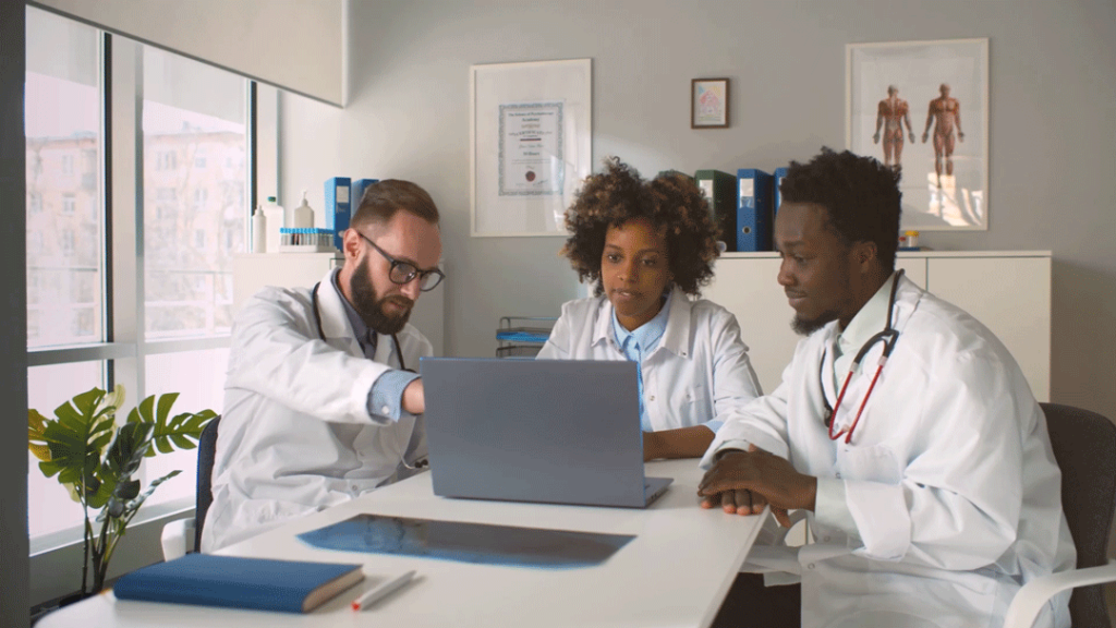 Three healthcare providers sit around a laptop reviewing options for continuous education for remote patient monitoring.