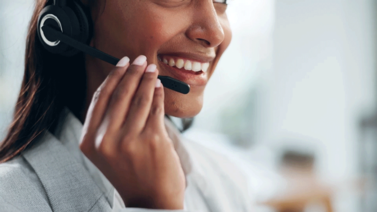 A nonclinical operator smiles while holding the microphone on her headset and helping a patient over the phone.