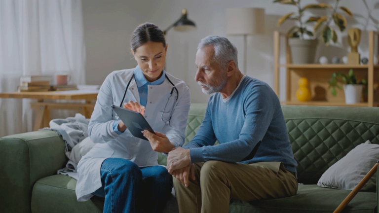 A doctor and their patient sit on a couch reviewing data on a tablet from remote patient monitoring.