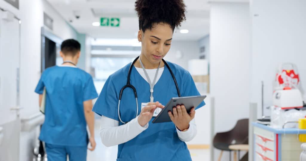 A hospital nurse uses a tablet to review patient data recorded with nurse triage software.