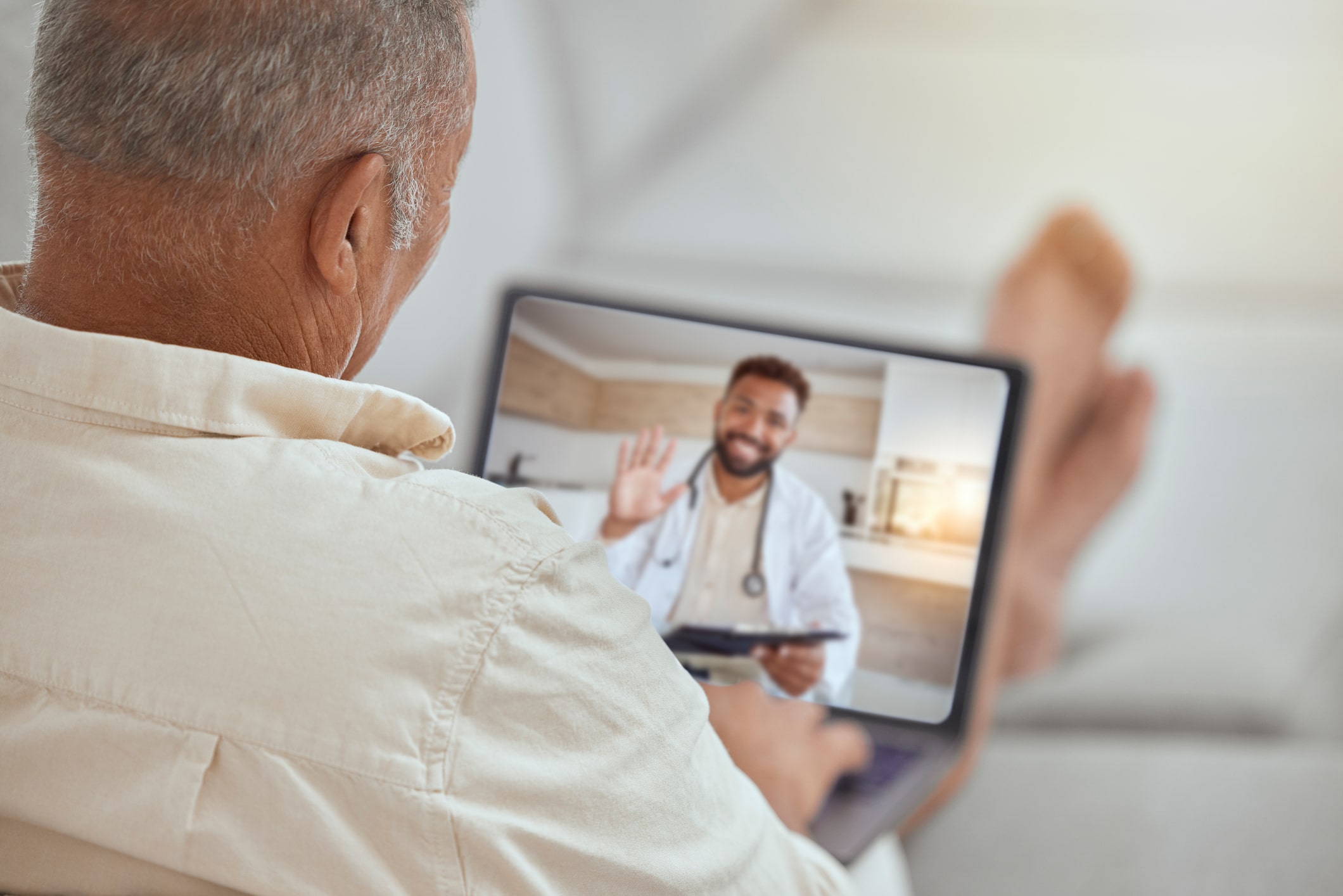 A patient rests at home while using their laptop to speak with their doctor through telehealth.