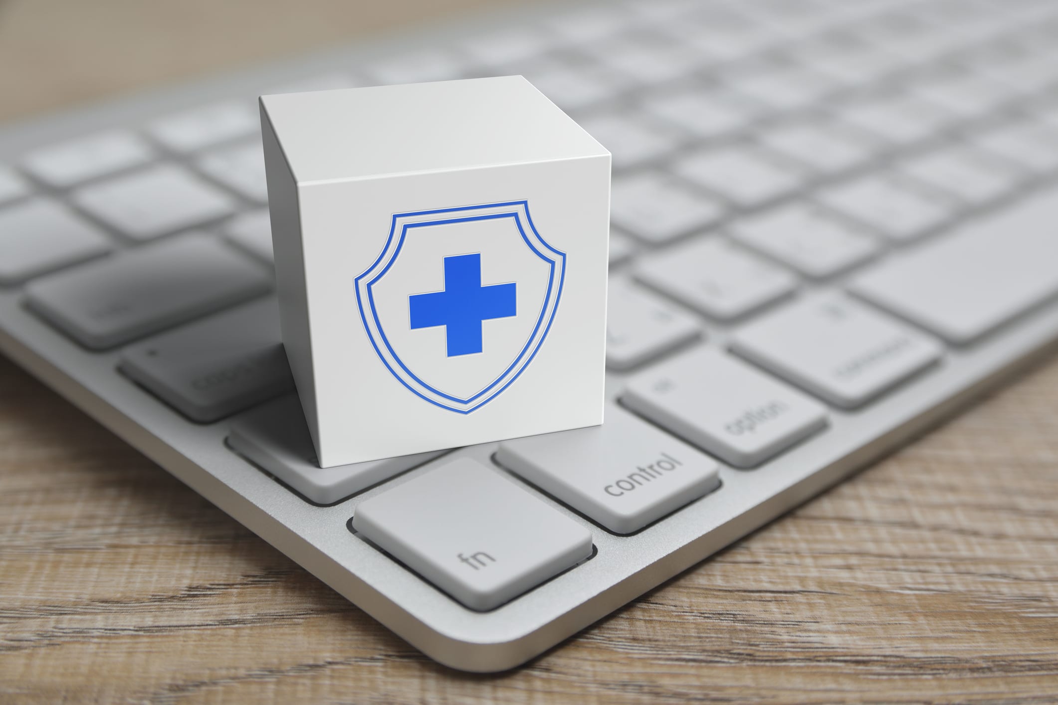 A block with a blue medical cross and shield is set on a keyboard, representing data security in remote patient monitoring.