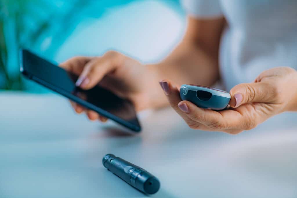 Remote patient monitoring concept: a patient uses a blood sugar testing device in conjunction with their smartphone.