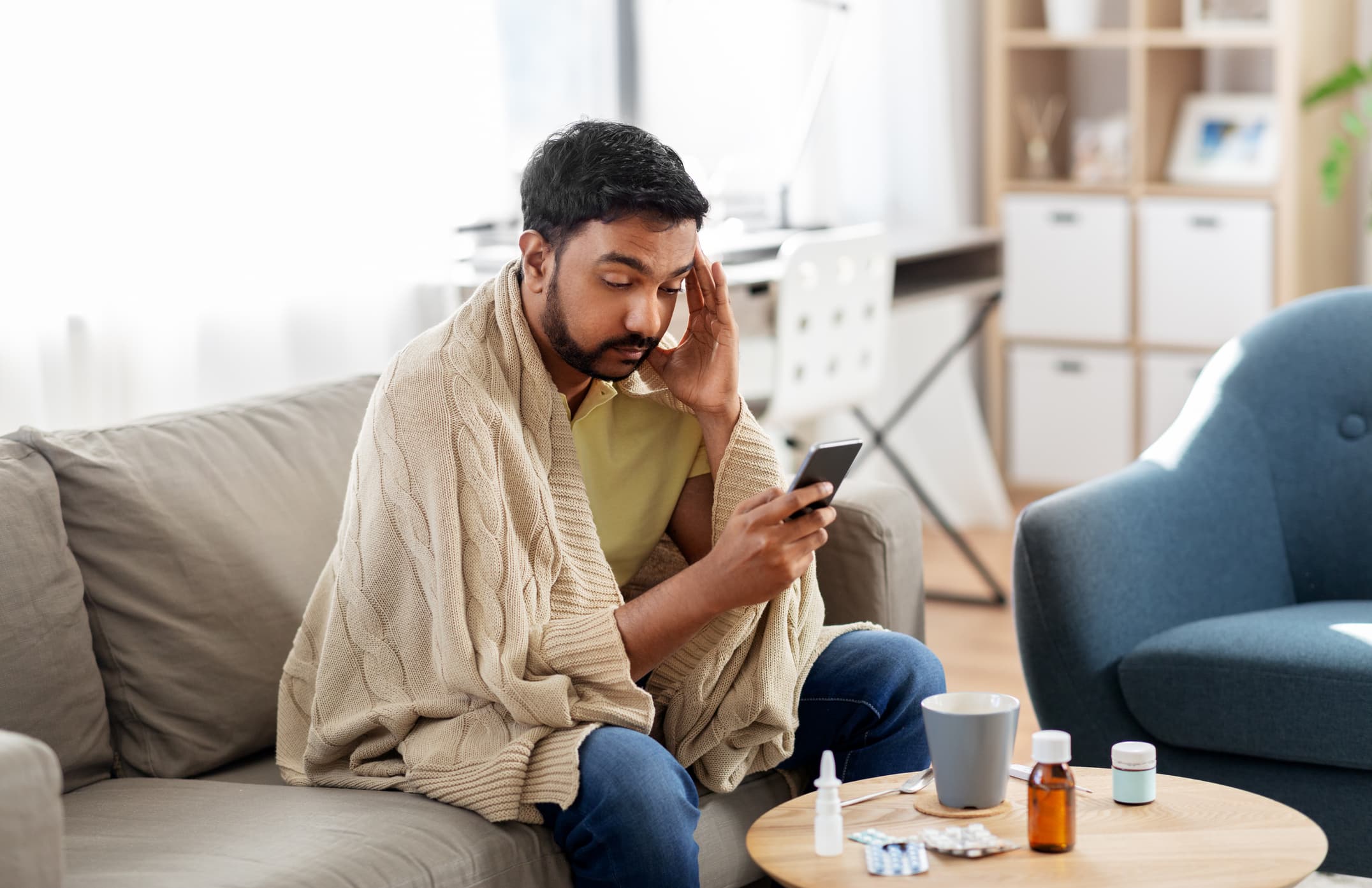 A sick patient sitting on his couch uses his smartphone to access automated medical answering services.
