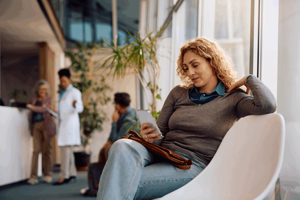 A woman uses her smartphone while sitting in a healthcare provider's waiting area.