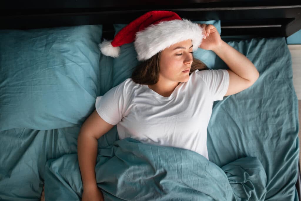 A person sleeps in a Santa hat, representing the importance of rest around the holidays as one of many healthy habits.