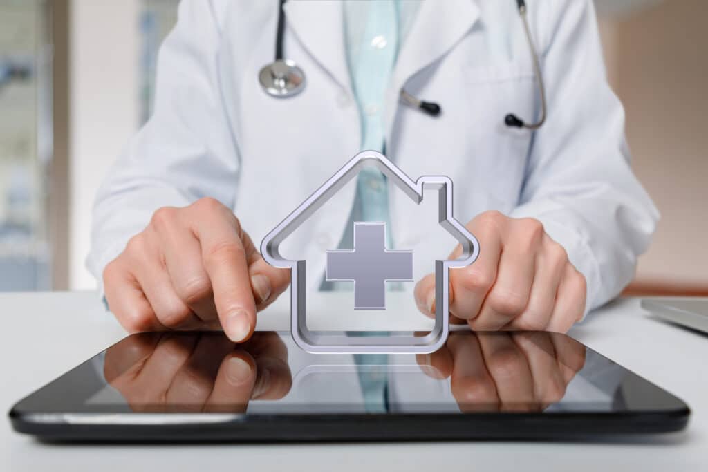 An icon representing home health care hovers above a tablet that a doctor uses to review remote patient monitoring data.