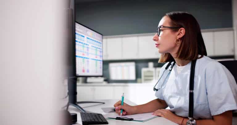 A nurse reviews triage software documentation on her workstation computer.