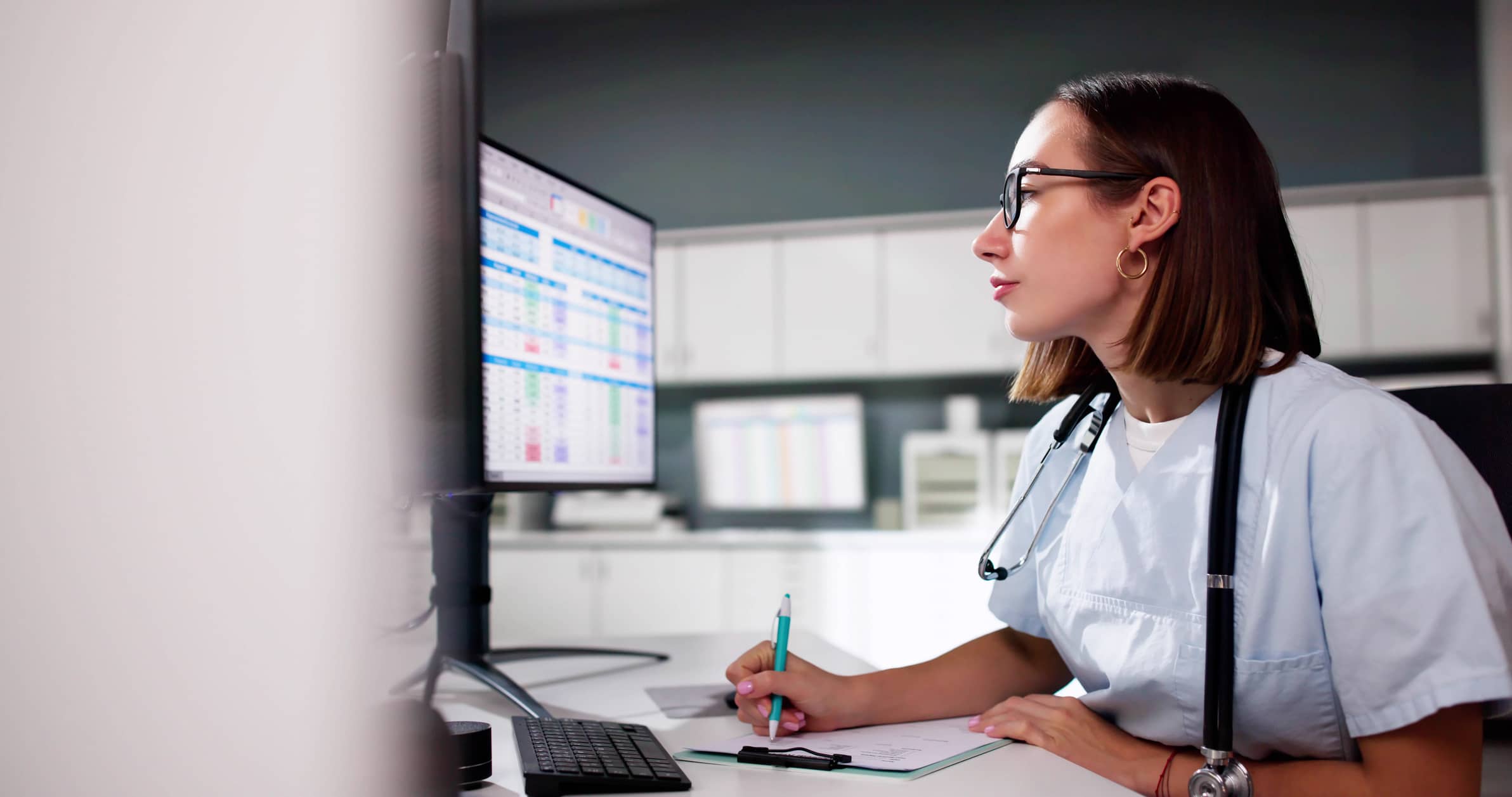 A nurse reviews triage software documentation on her workstation computer.