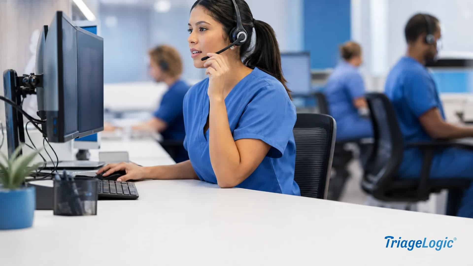 Registered nurse at a triage call center workstation reviewing patient information on dual monitors while speaking via headset.