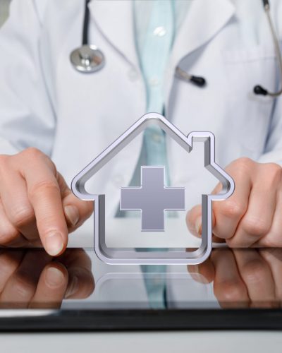 An icon representing home health care hovers above a tablet that a doctor uses to review remote patient monitoring data.