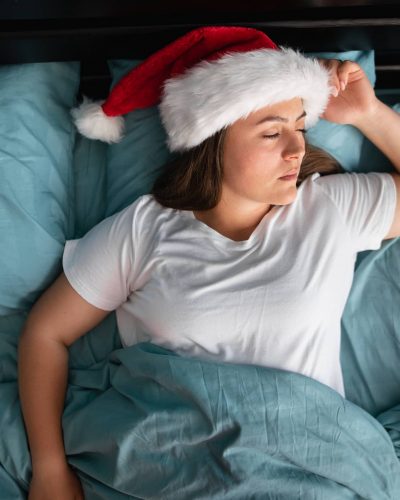 A person sleeps in a Santa hat, representing the importance of rest around the holidays as one of many healthy habits.