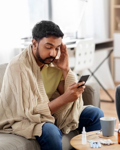 A sick patient sitting on his couch uses his smartphone to access automated medical answering services.