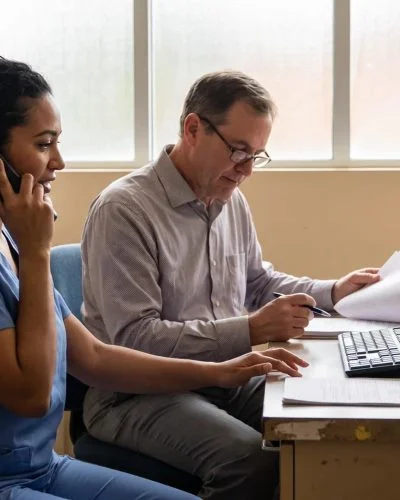 Registered nurse at a clinic desk taking a patient call, illustrating how nurse lines support healthcare access and cost savings.